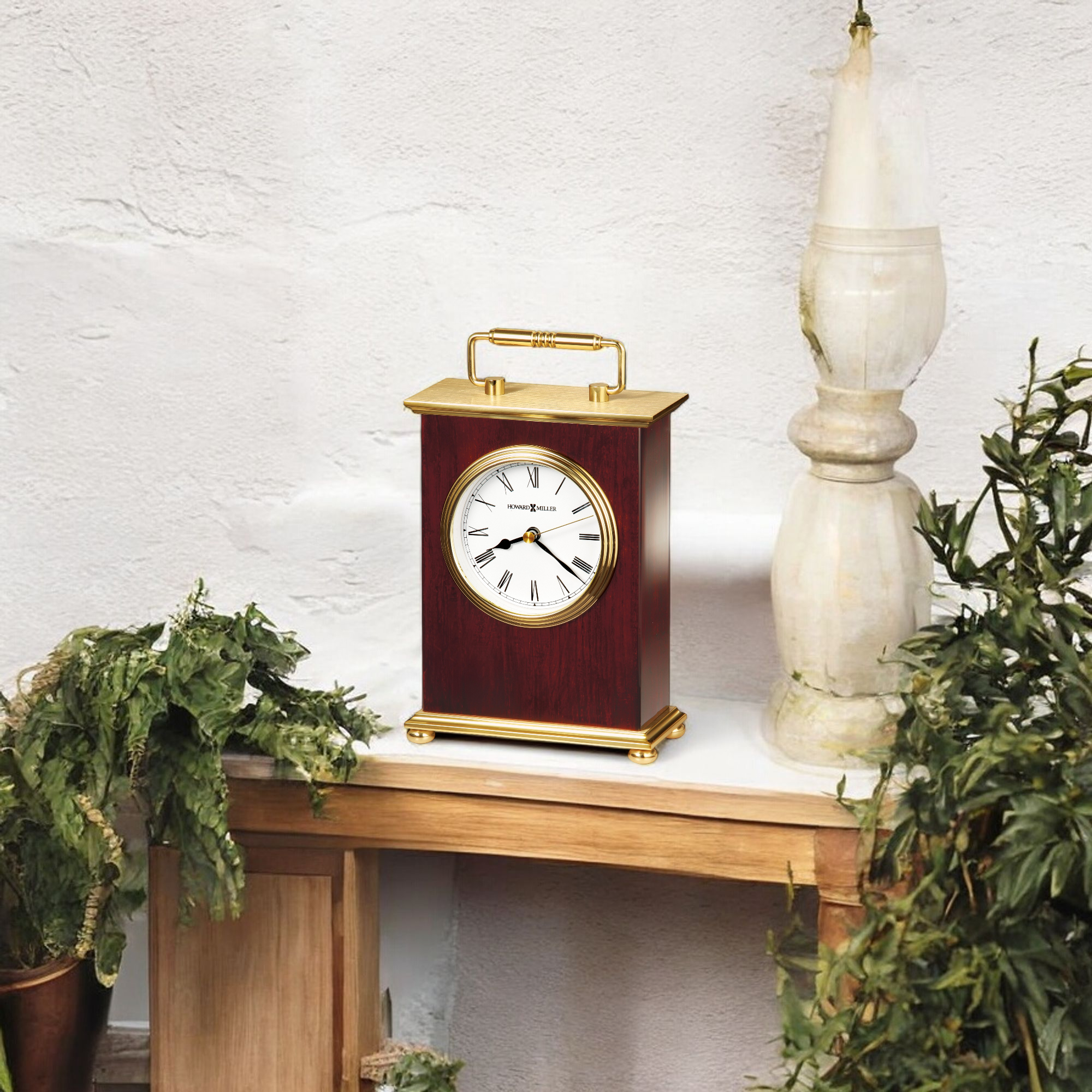A vintage-style clock on a wooden table surrounded by greenery.
