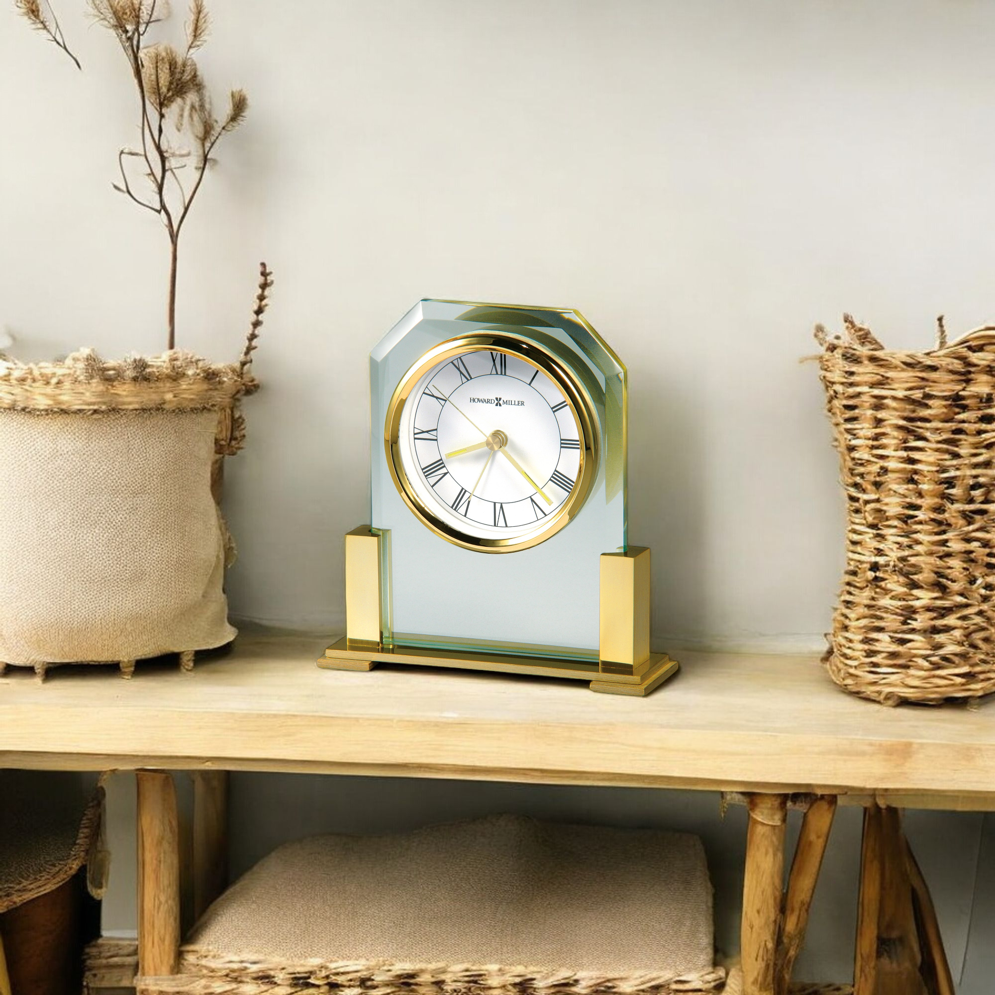 A stylish gold and glass clock on a wooden shelf next to decorative woven baskets.