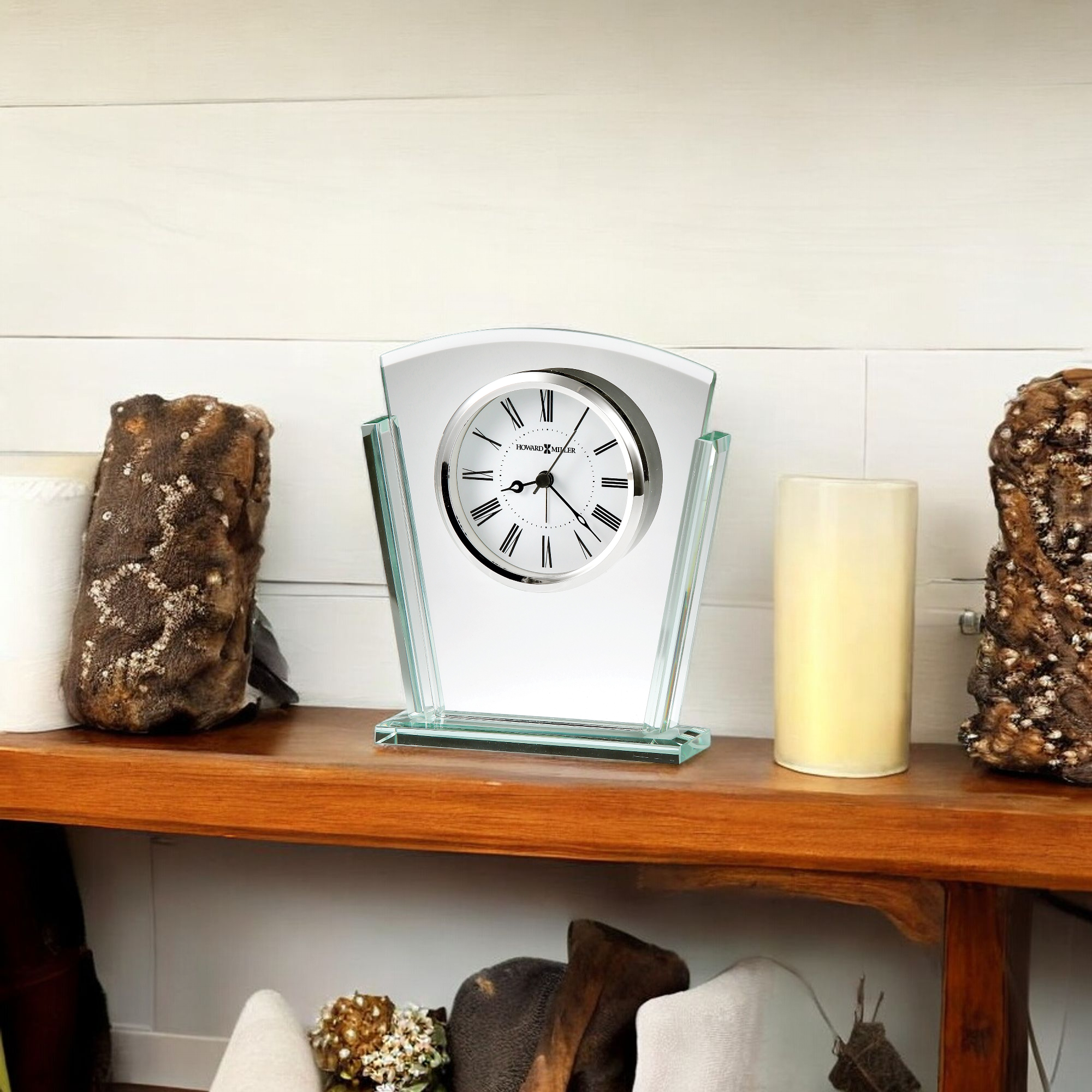 A decorative clock on a wooden shelf surrounded by candles and textured objects.