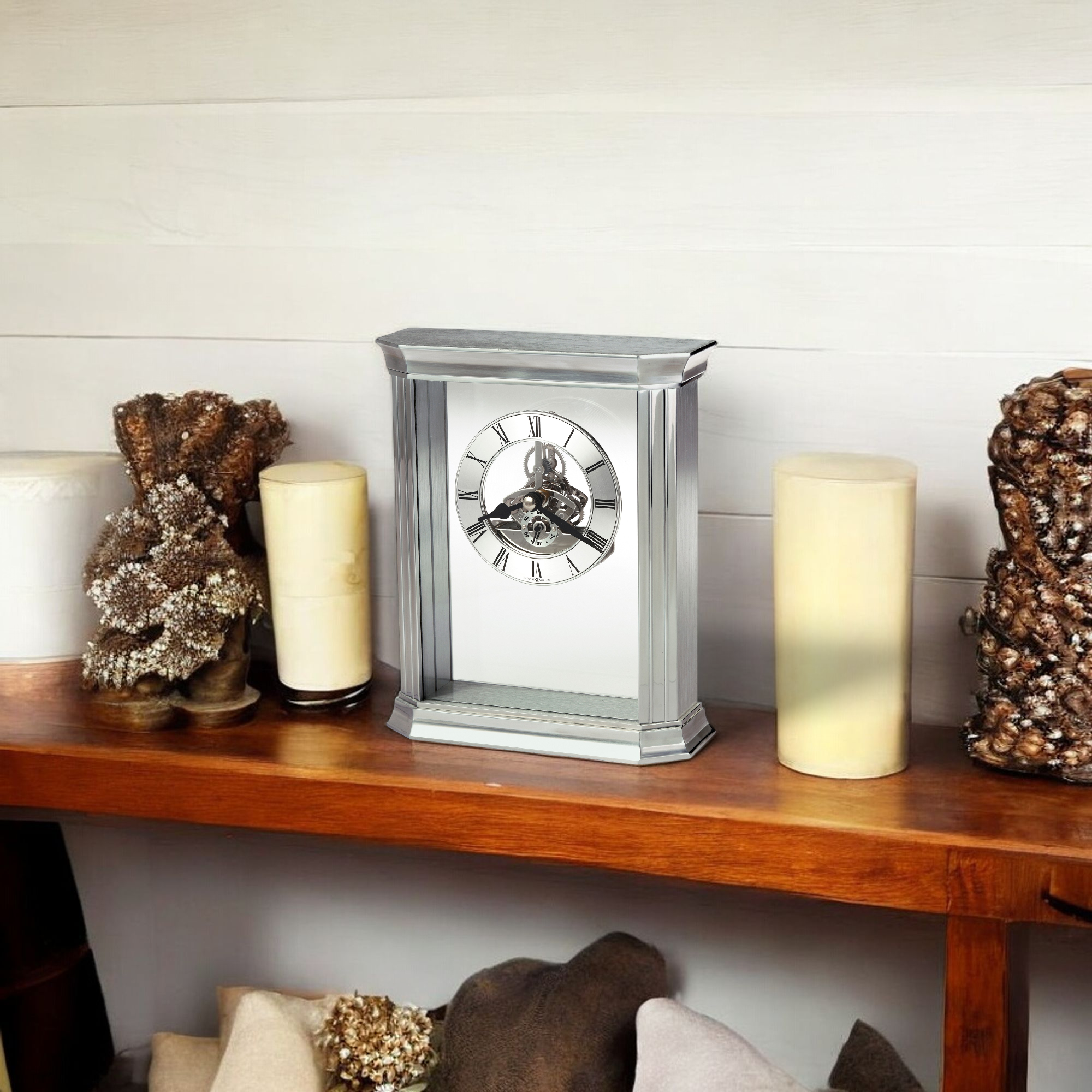 A modern clock displayed on a wooden shelf alongside decorative candles and natural elements.