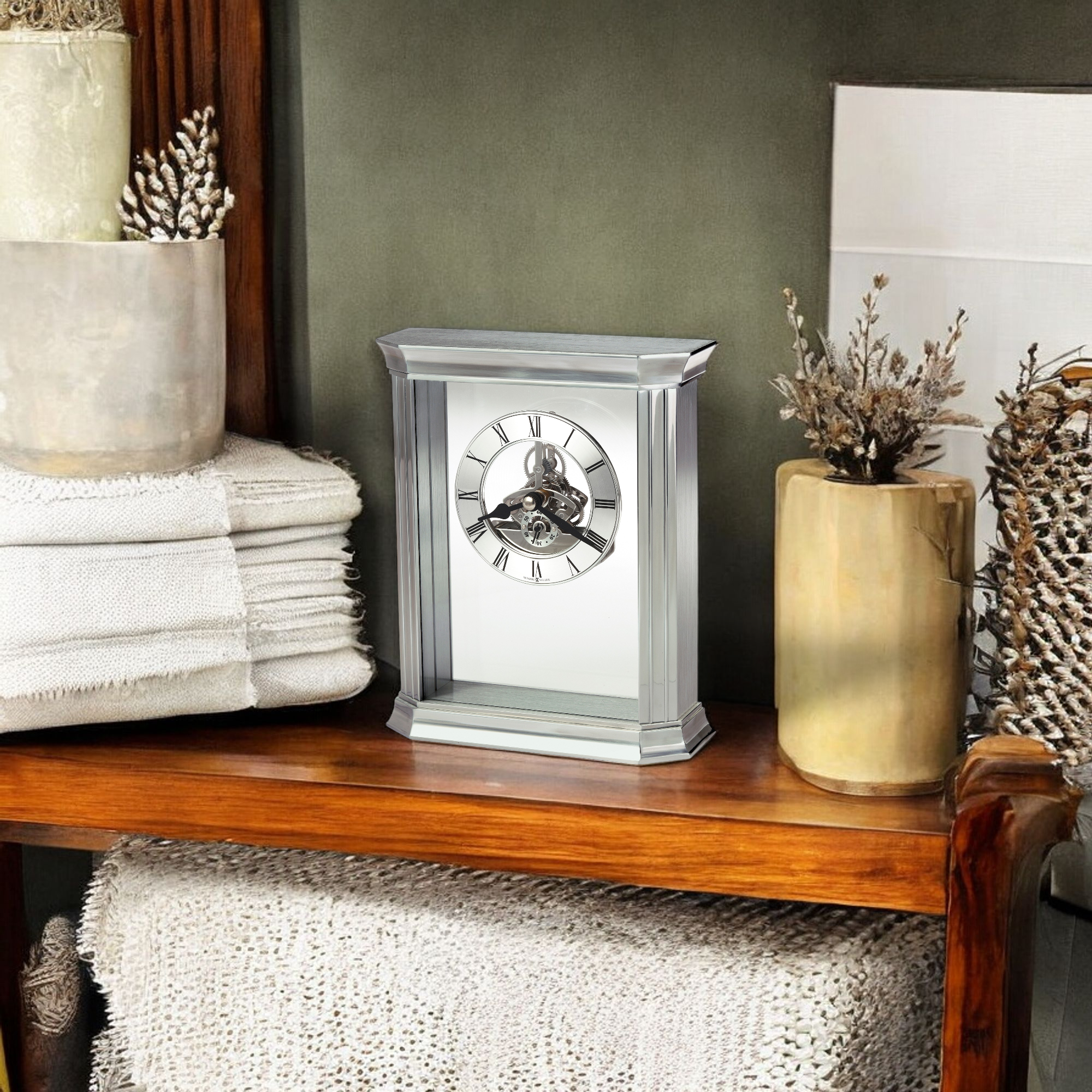 A decorative silver clock displayed on a wooden shelf with neutral decor.