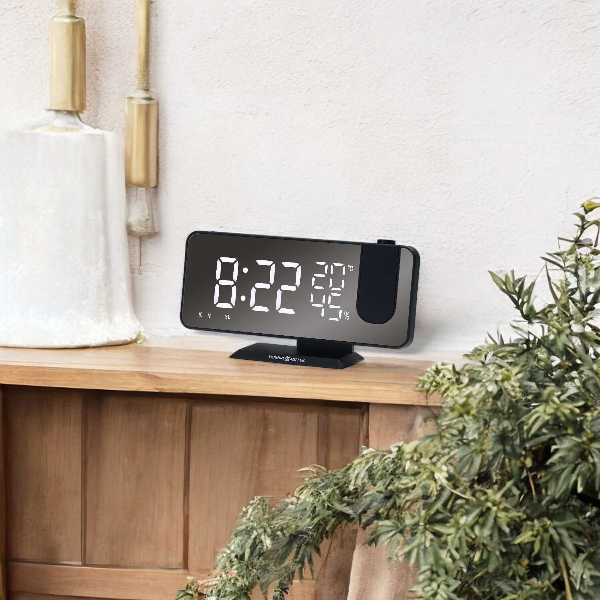 A digital alarm clock displaying the time 8:22 on a wooden shelf with a plant and decorative items.