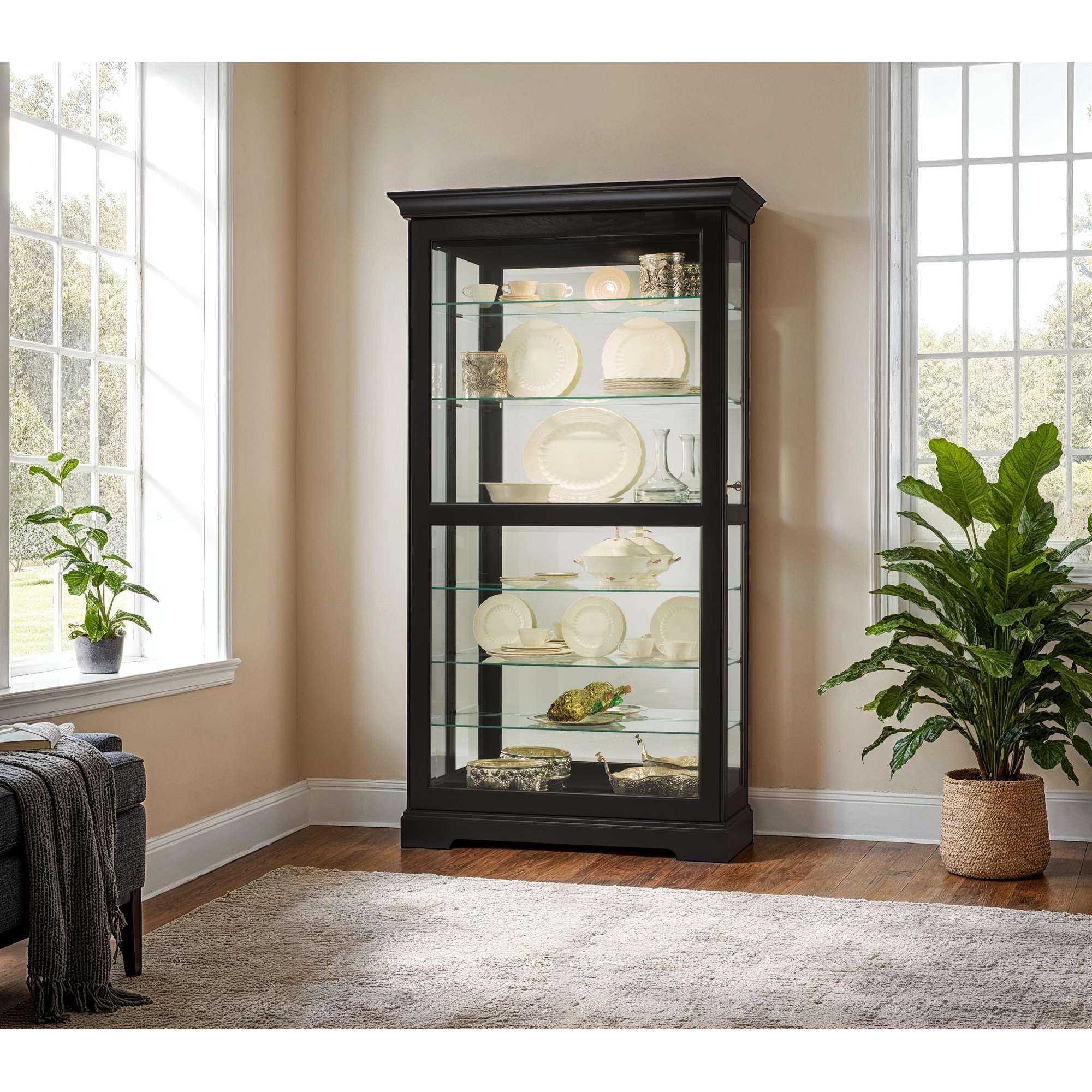 A black display cabinet with glass shelves showcasing decorative items, positioned near large windows and a potted plant.