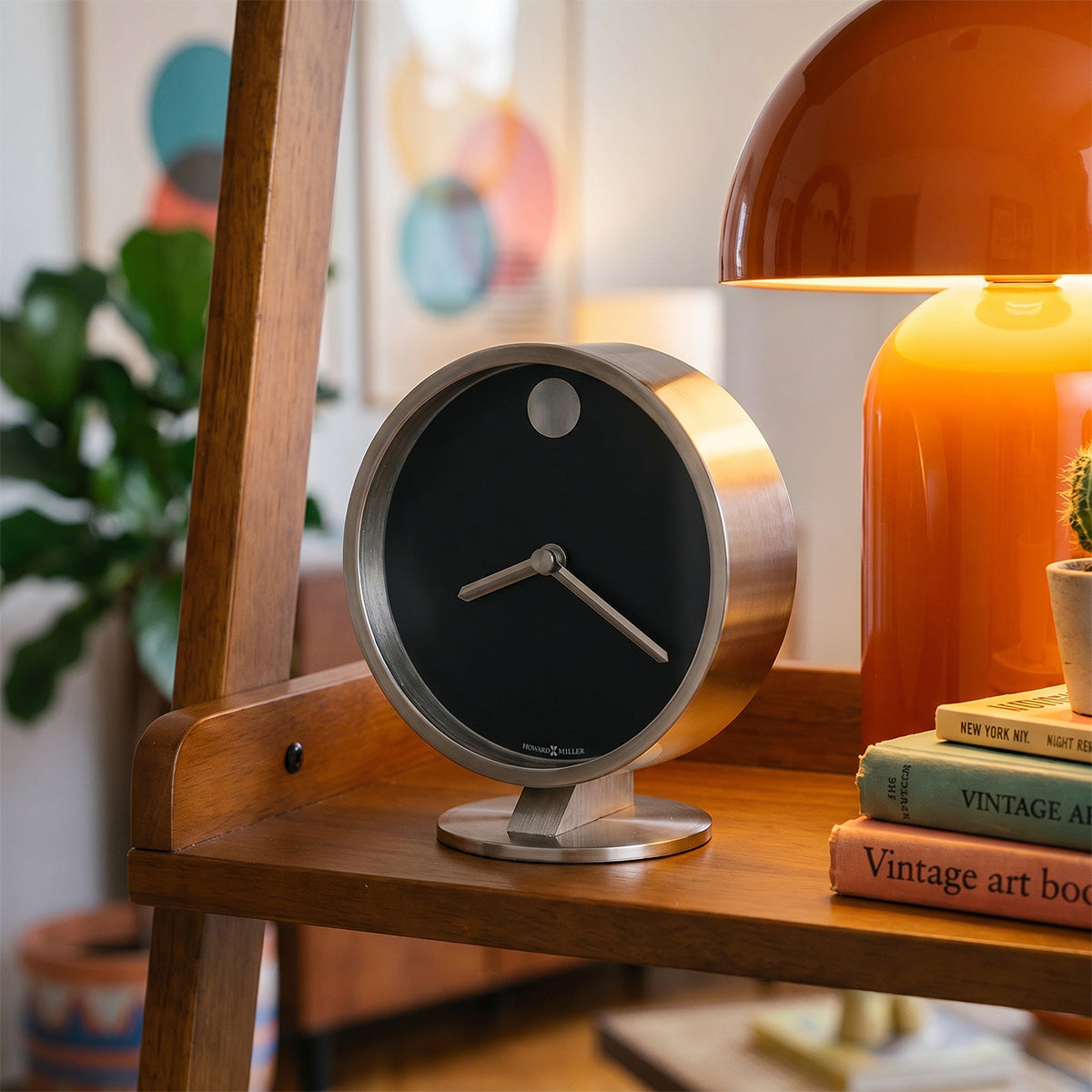 Tabletop clock on a wooden shelf with books and a lamp in a cozy room setting