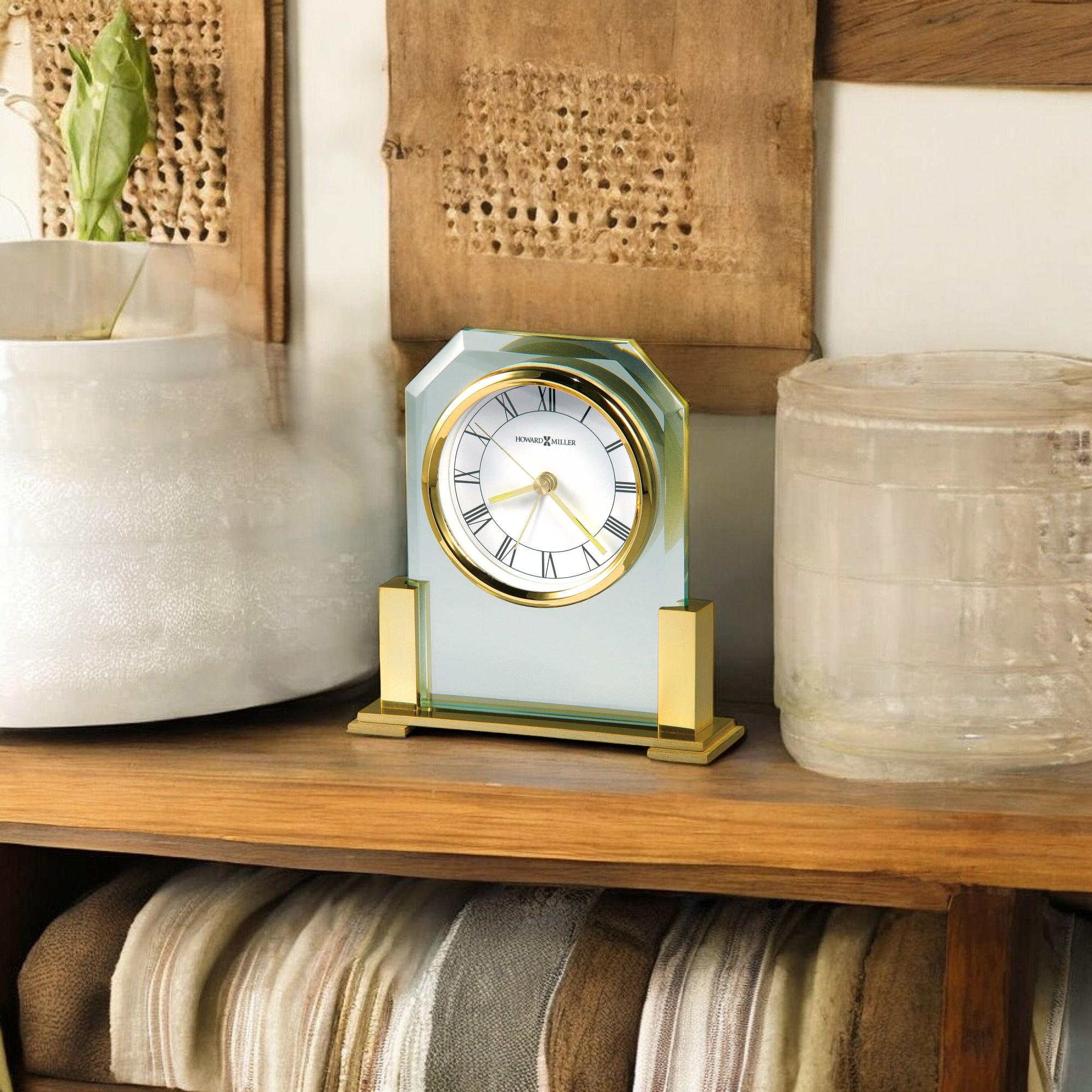 A stylish gold-accented clock displayed on a wooden shelf with various decorative items.