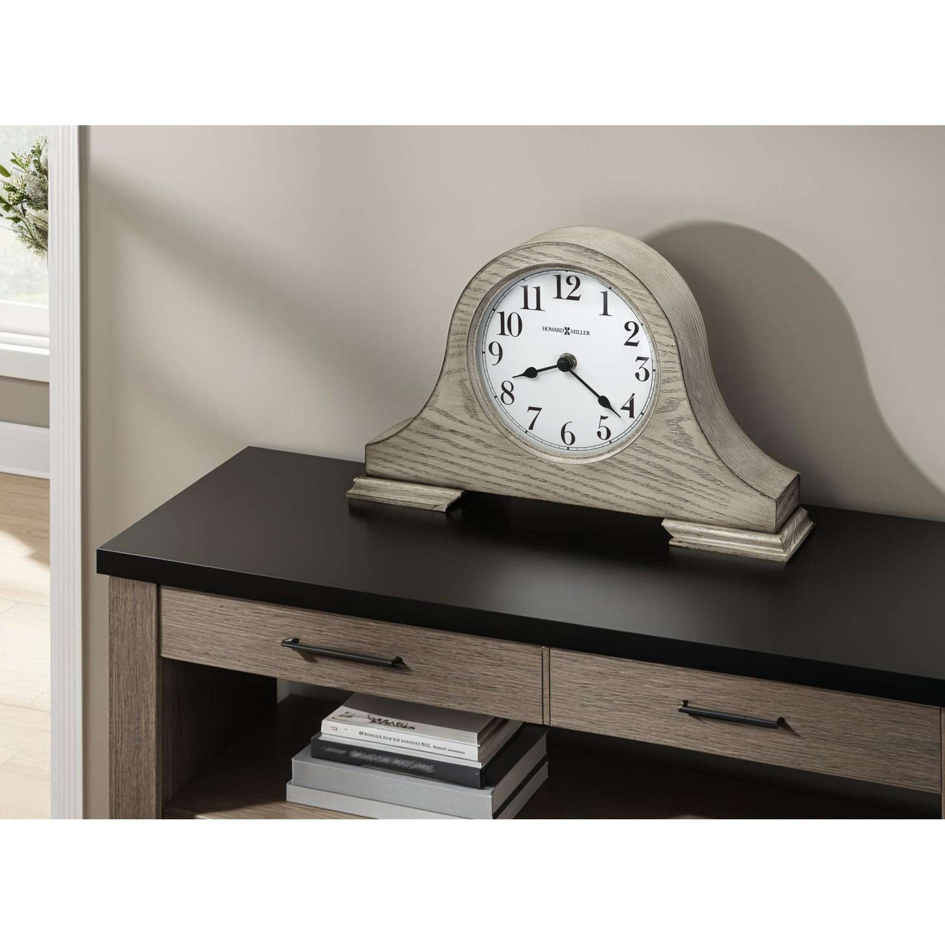 A decorative clock on a black tabletop with wooden drawers.