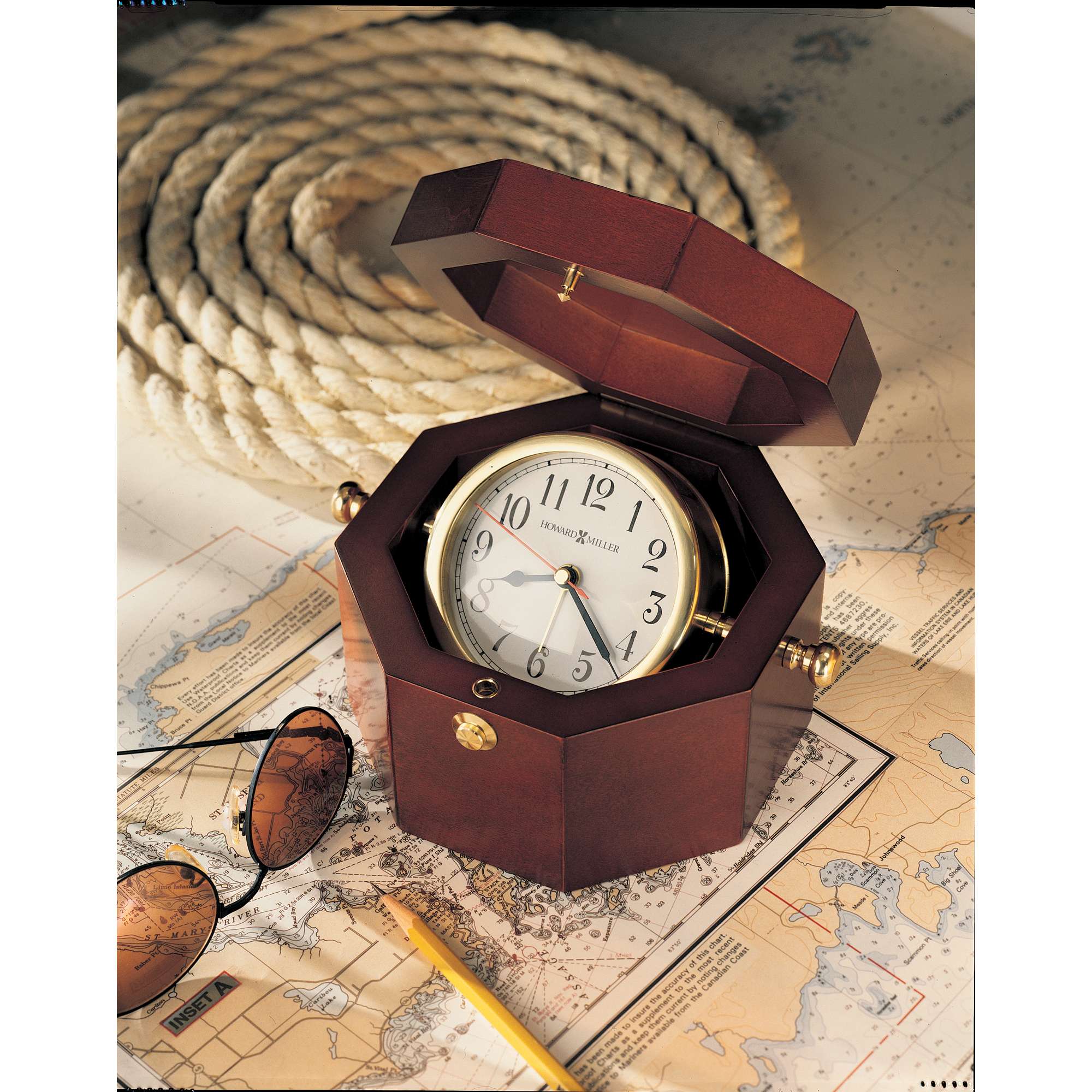 A wooden octagonal clock displayed open on a vintage map with sunglasses and a pencil.