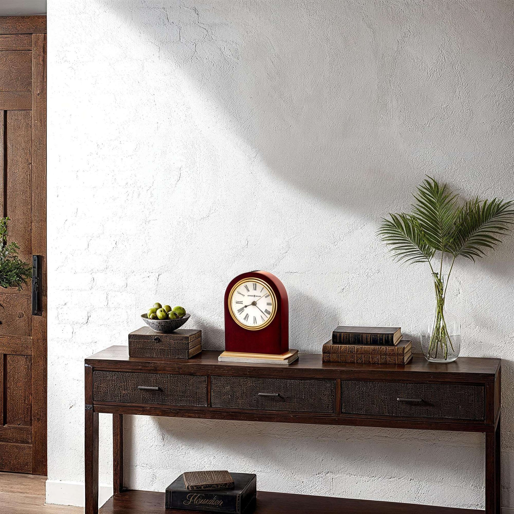 A wooden console table with a clock, decorative bowls, and a potted plant against a textured white wall.