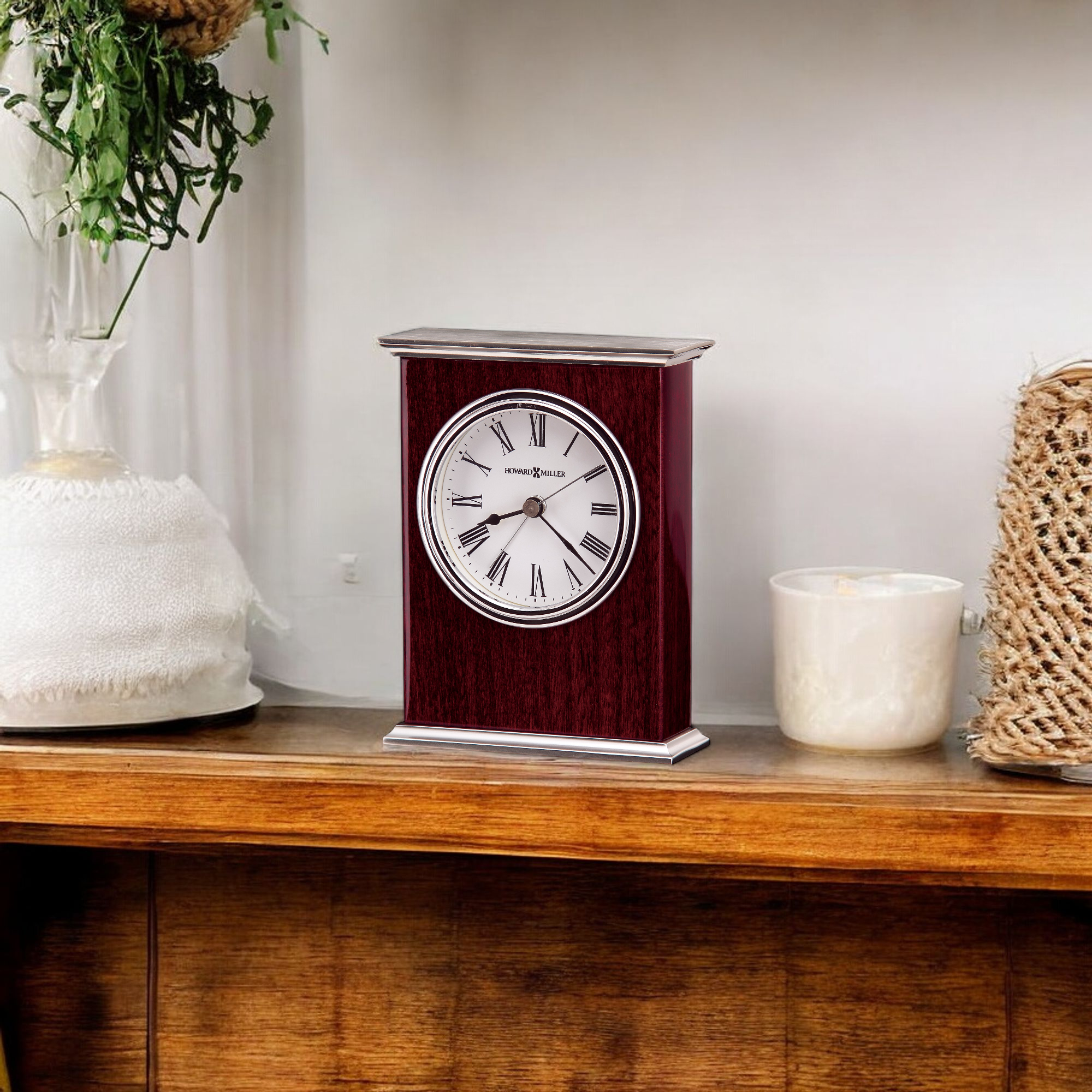 A vintage-style clock on a wooden shelf, next to a candle and decorative items.