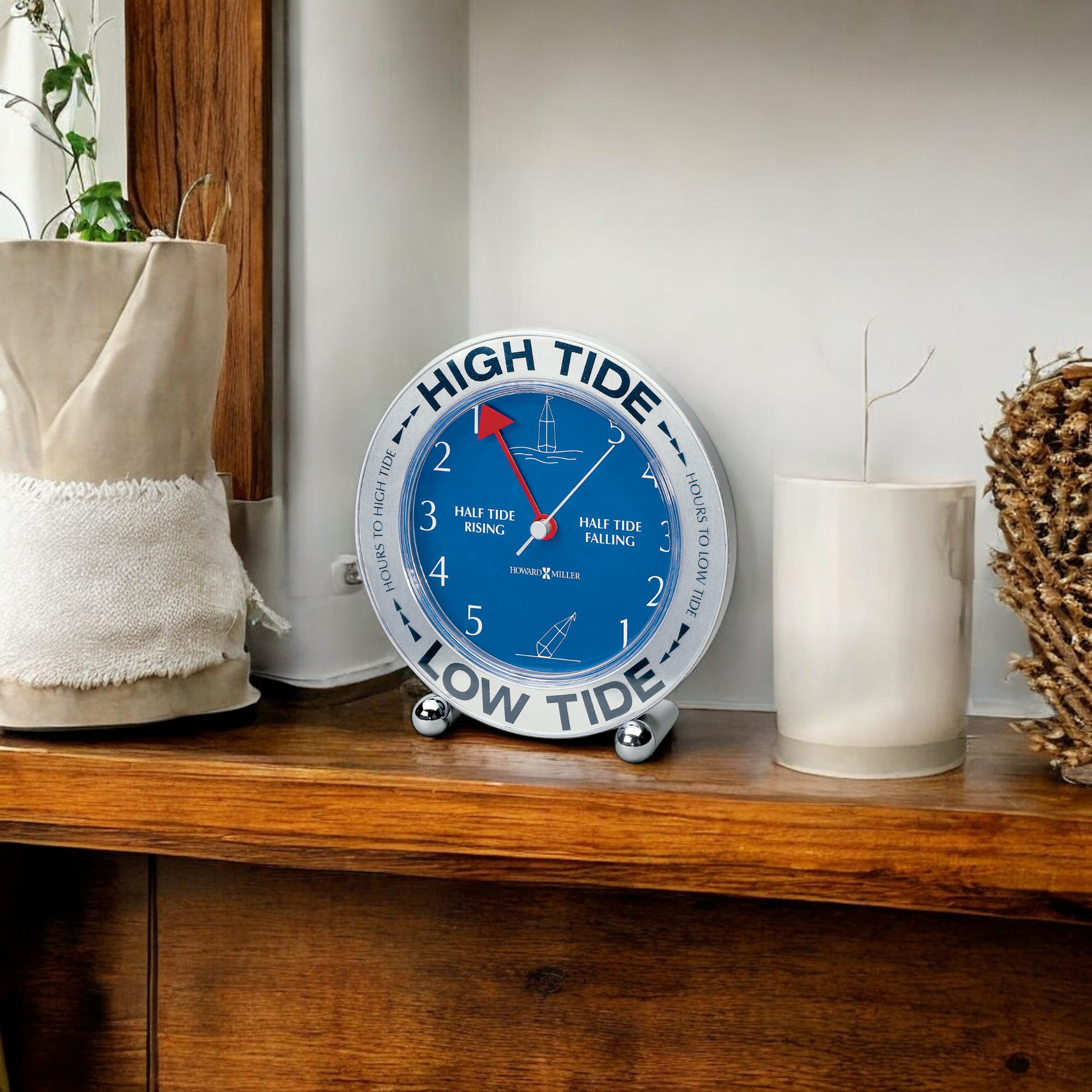 A decorative tide clock indicating high and low tide on a wooden shelf with potted plants.