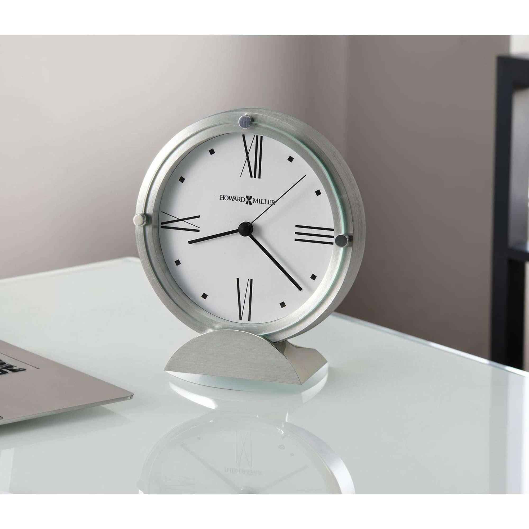 A sleek desk clock with a white face and Roman numerals, placed on a glass surface.