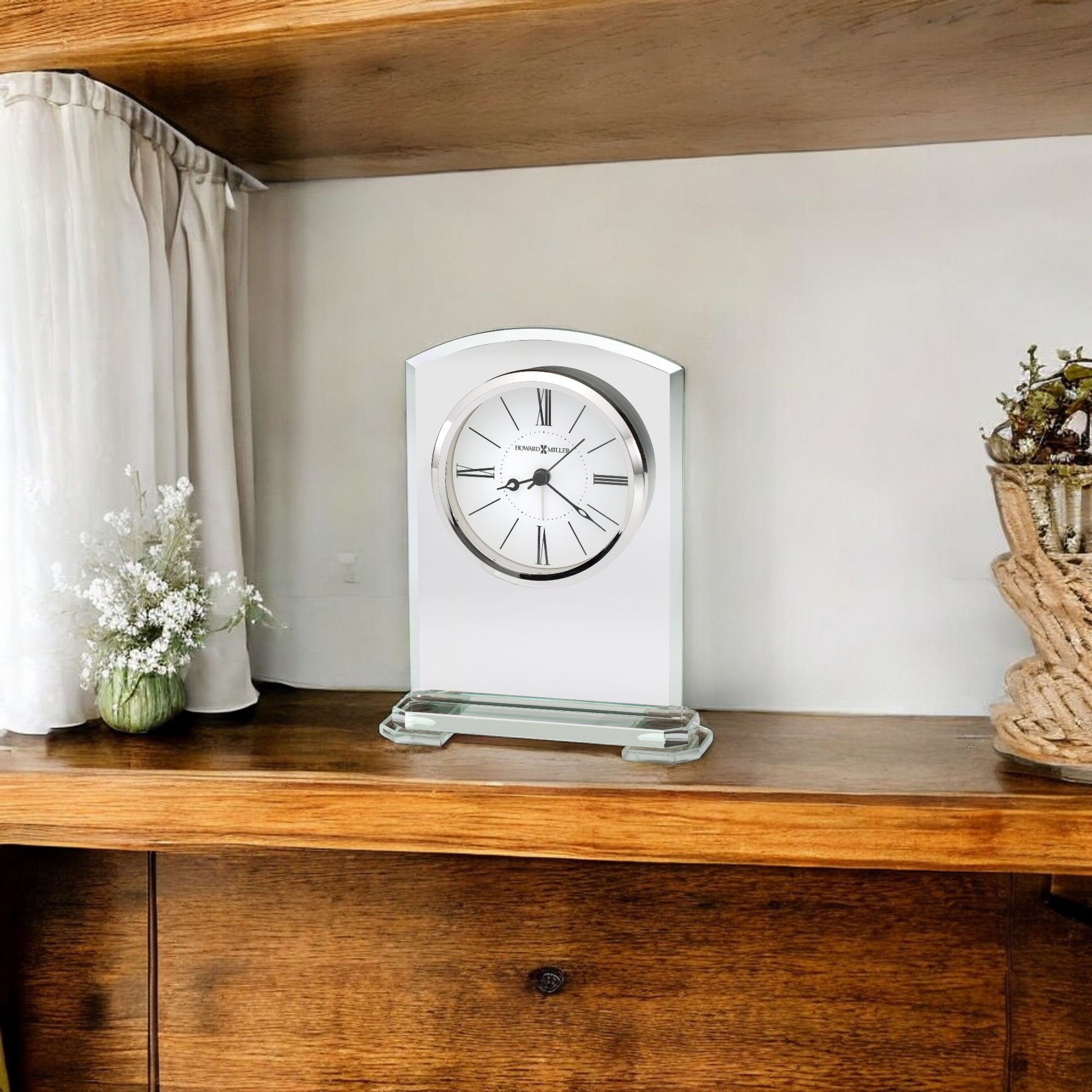 A decorative clock displayed on a wooden shelf beside a small vase of flowers.