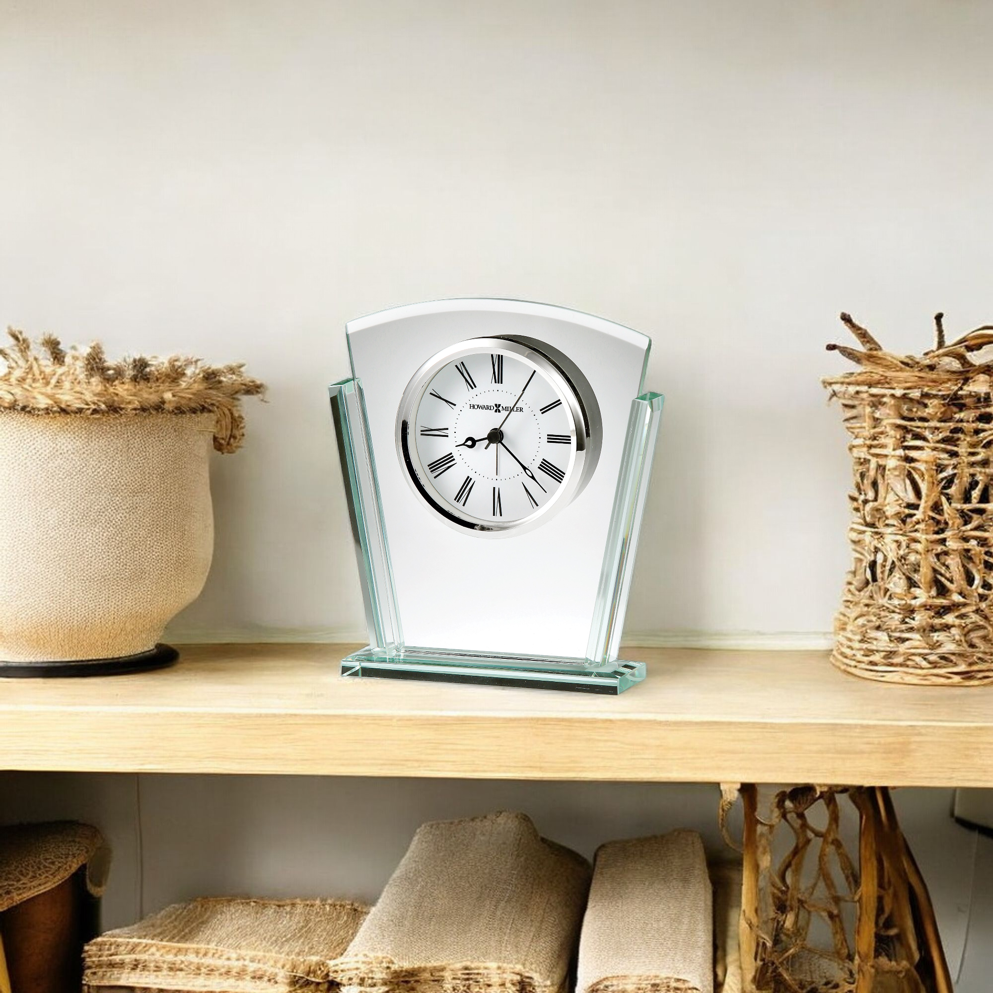A decorative silver and glass clock displayed on a wooden shelf alongside woven baskets.