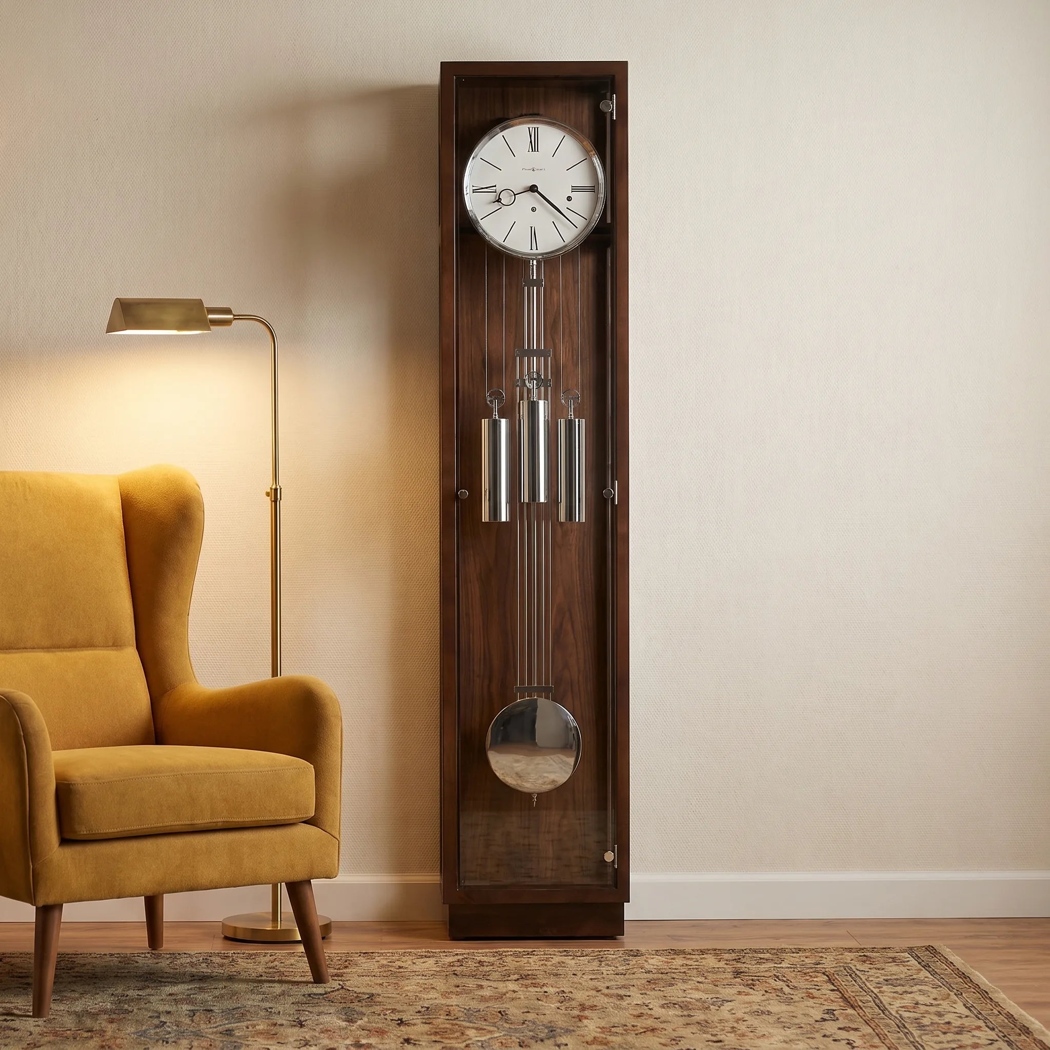 A tall dark wood grandfather clock with a white clock face and silver pendulums stands in a room next to a mustard yellow armchair and a floor lamp.