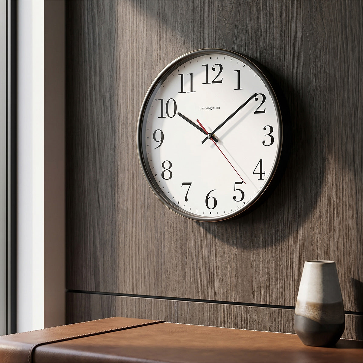 Wall clock on a wooden wall with a vase on a table below.