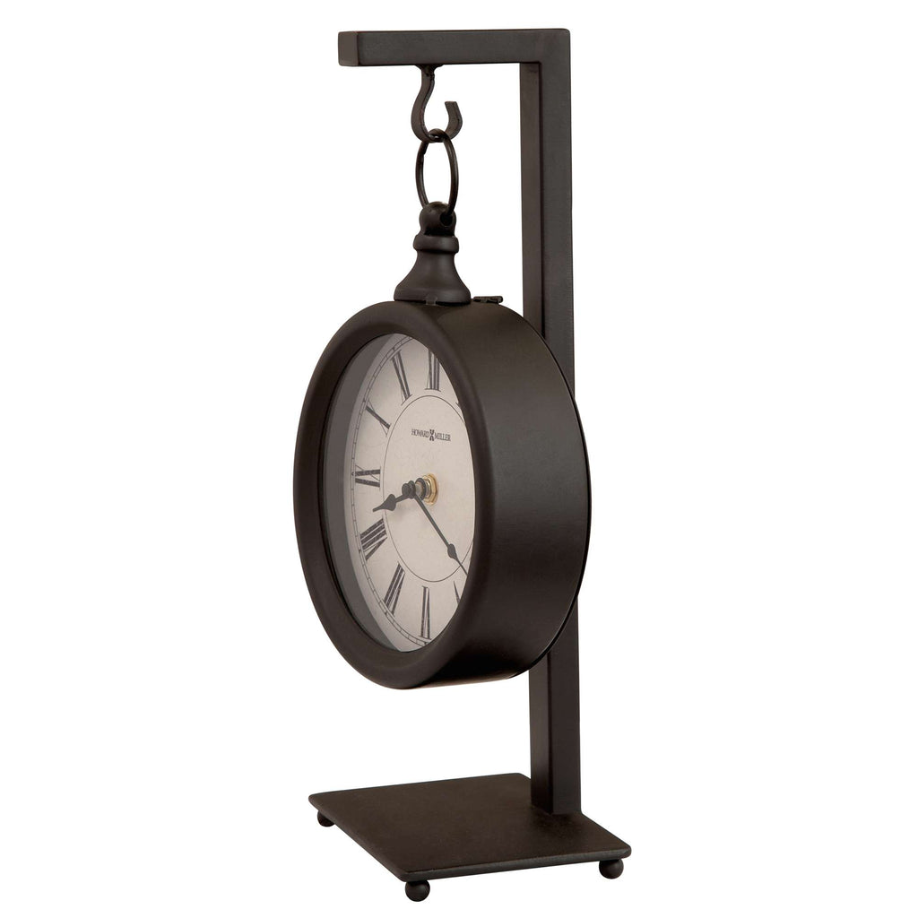 A modern black tabletop clock with a round face and Roman numerals, supported by a sleek metal stand.