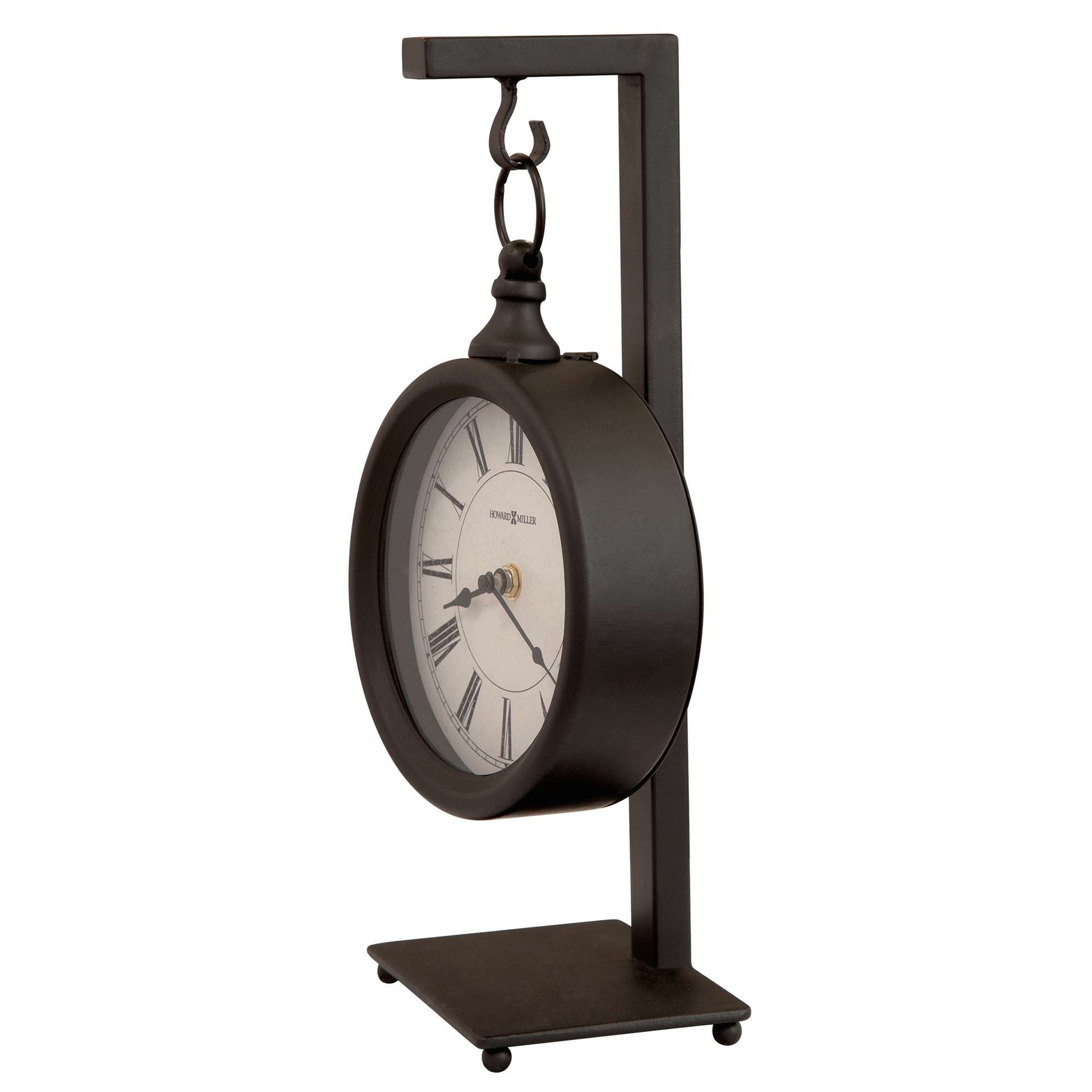 A modern black tabletop clock with a round face and Roman numerals, supported by a sleek metal stand.