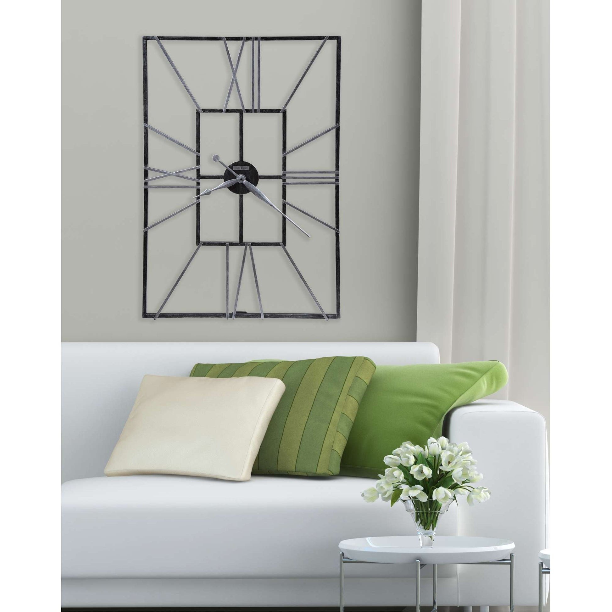 Modern wall clock on a light grey wall above a white sofa with decorative pillows and a small vase of flowers.