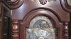 Close-up of an ornate wooden grandfather clock with a detailed clock face.