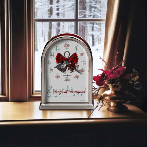 A decorative clock with a red bow and the text 'Songs of Christmas' on a windowsill with snowy scenery outside.